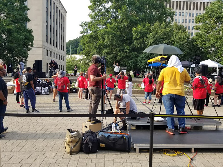 Dominic Desantos, center in red shirt, finds the right angle for Camera 1. Below him, audio tech Brian Garfield monitors the levels. In the background, left, camerman Tim Gordon can be seen getting reverse coverage.