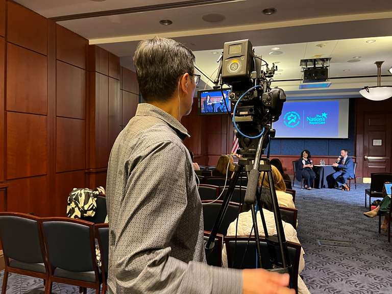 Producer/Director Ben Wong lines up the shot of NCES Commissioner Dr. Peggy Carr and board member Patrick Kelly at the Examining the Past, Present, and Future: 2022 Nation's Report Card in U.S. History and Civics event.